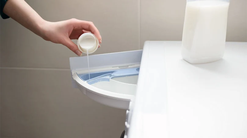 a woman pouring a fabric softener in a washing machine