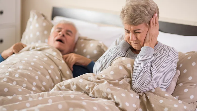 Una imagen de una pareja de ancianos en la cama donde el marido ronca y no deja dormir a la mujer