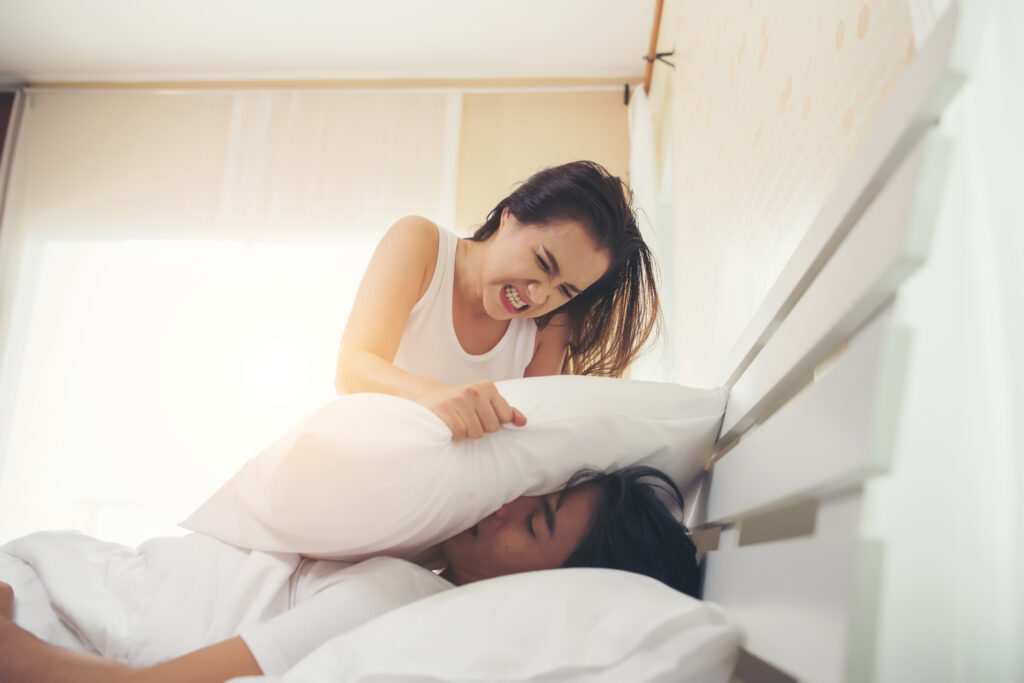 Una imagen de una mujer tapando la boca de su marido con una almohada para que deje de roncar.