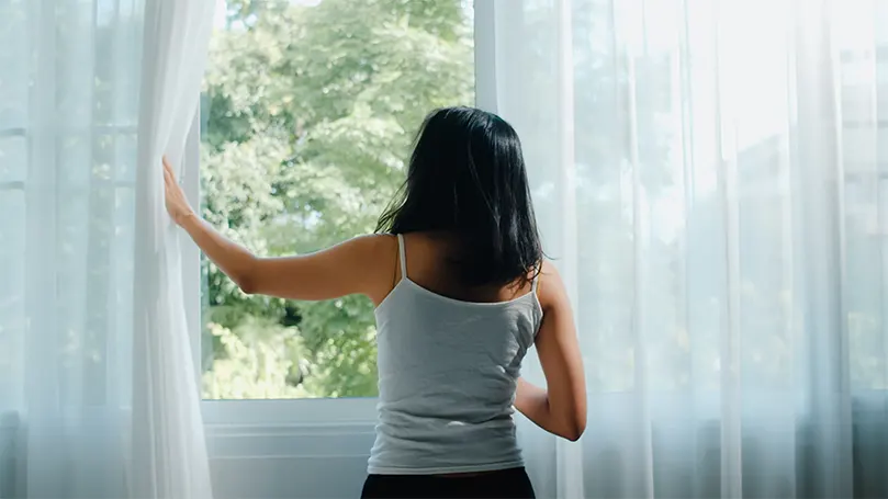 Una imagen de una mujer abriendo la ventana y dejando entrar el aire fresco