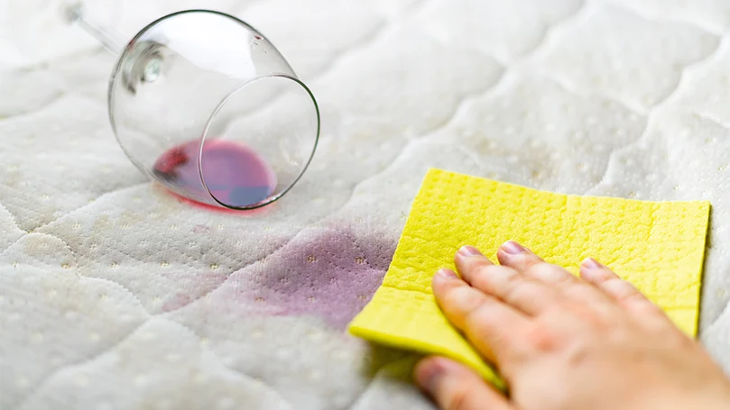 una mujer secando una mancha de vino en la funda de un colchón.