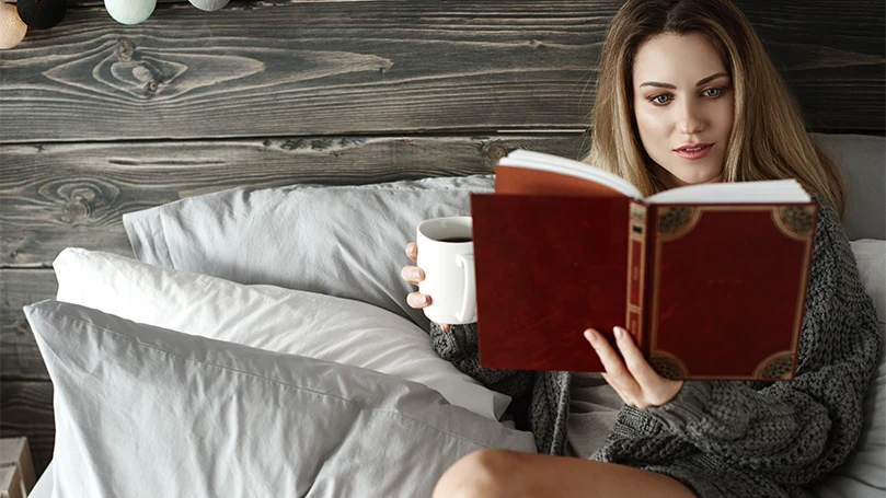 Imagen de una mujer leyendo un libro en la cama