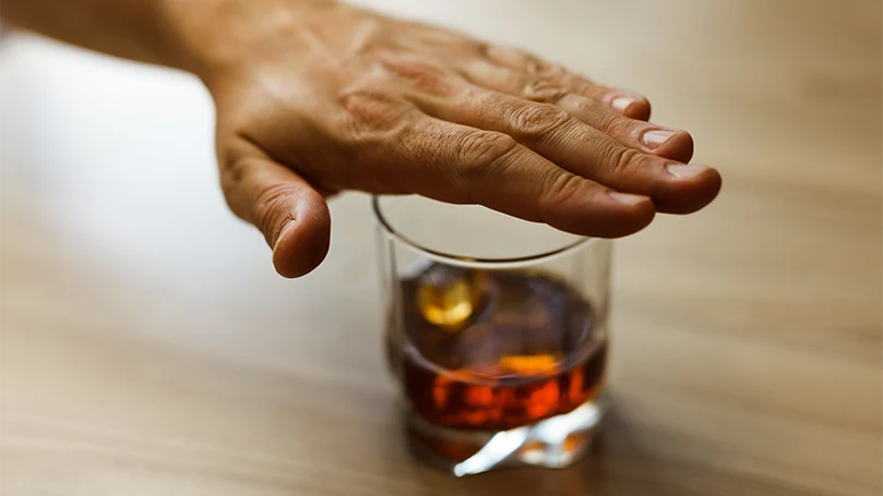 Una mano masculina sobre el vaso de alcohol.