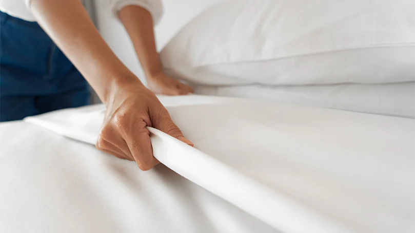 An image of a female setting up a sheet on a bed.