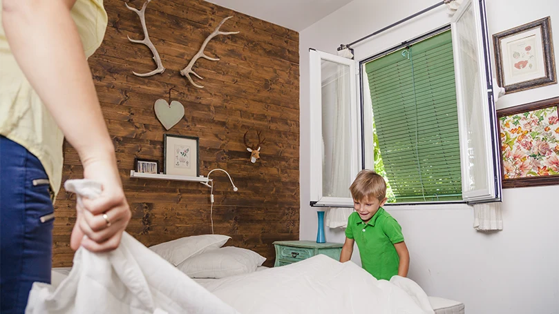 an image of a mom teaching her son how to make a bed