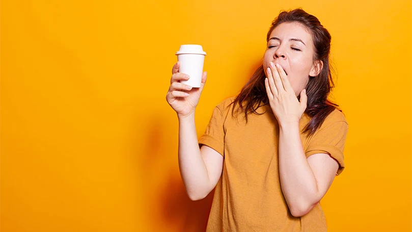 Una mujer somnolienta con una taza de café en la mano.