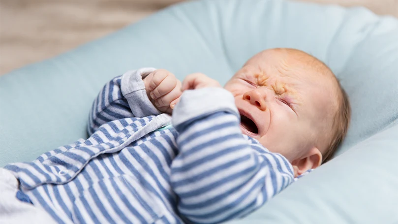 An image of a baby crying in cot bed mattress.