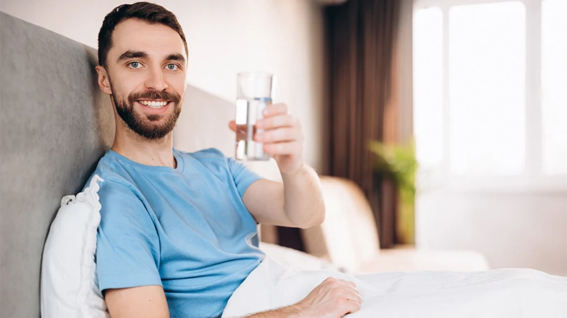 Imagen de un hombre bebiendo un vaso de agua en su cama antes de acostarse.