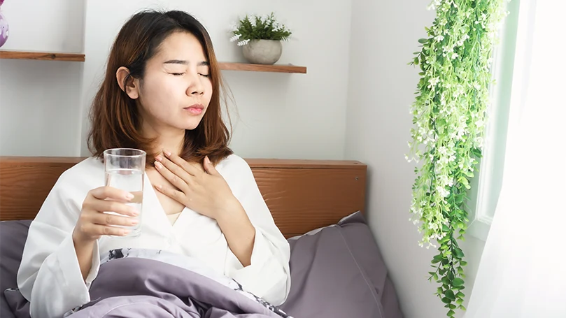 Imagen de una mujer asiática joven y enferma bebiendo agua en la cama antes de dormir.