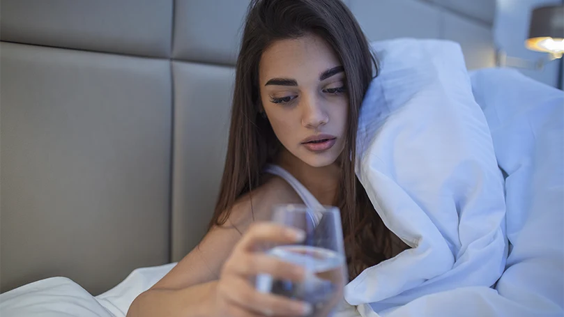 Imagen de una mujer joven tomando un vaso de agua en la cama.