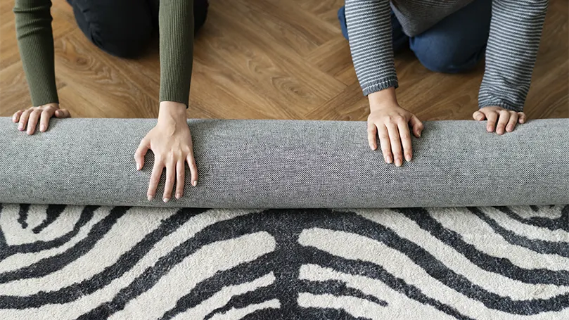 Una pareja que pone una alfombra debajo de la cama para evitar que se deslice.