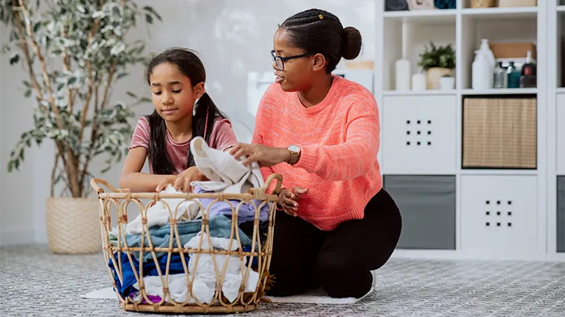 Imagen de una madre y su hija preparando pijamas y ropa para lavar.