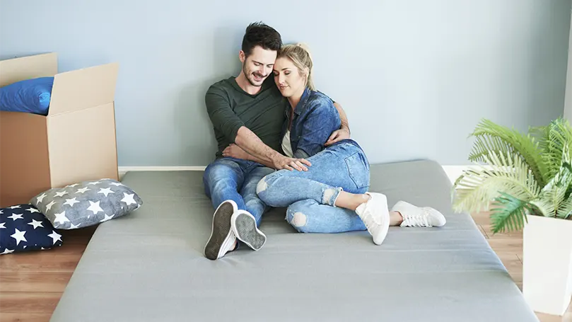 A young couple hugging and laying on a new mattress in a box they've just unpacked.