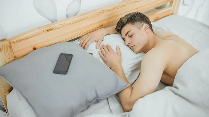 Imagen de un hombre joven y guapo durmiendo profundamente en su cama.