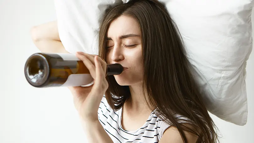 Imagen de una mujer bebiendo alcohol en la cama.