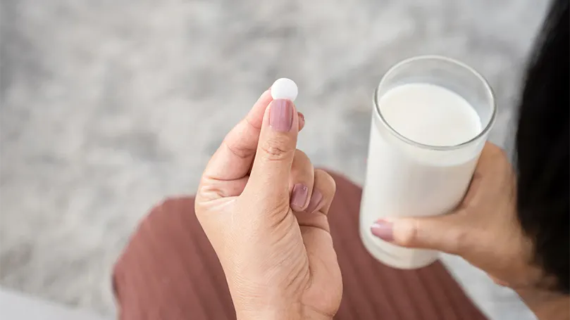 Una mujer tomando una pastilla de melatonina con un vaso de leche.