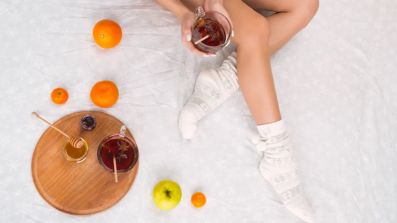 An image of a woman in socks on bed drinking tea.