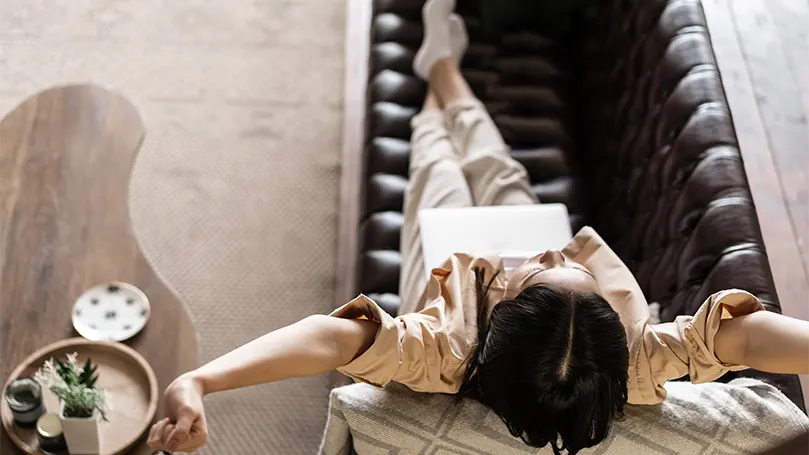 An image of a woman laying down on a couch with laptop.