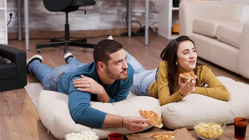 Una imagen de una pareja en el suelo comiendo pizza.