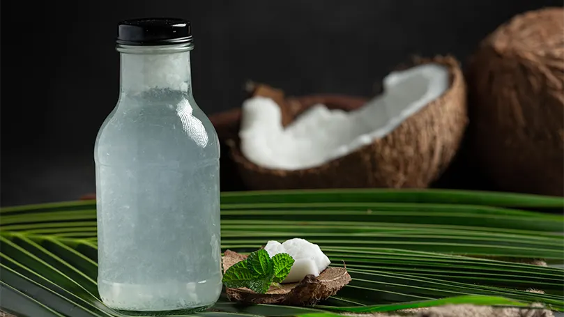 Una imagen de una botella de agua de coco delante de un coco roto