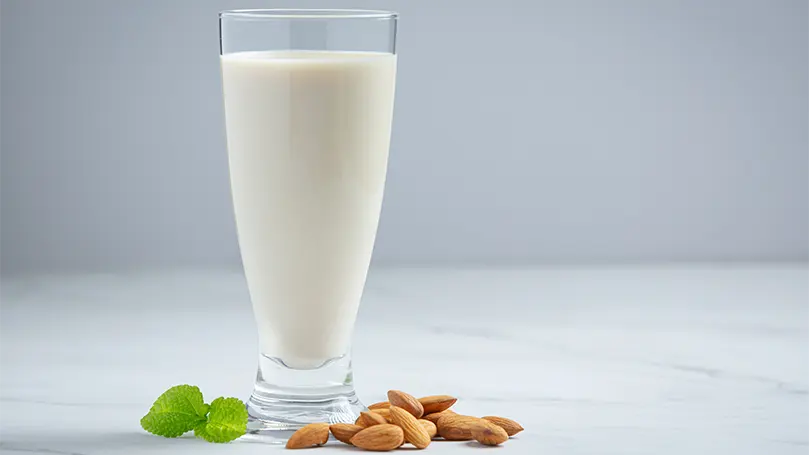 Una imagen de leche de almendras en un vaso con almendras a un lado