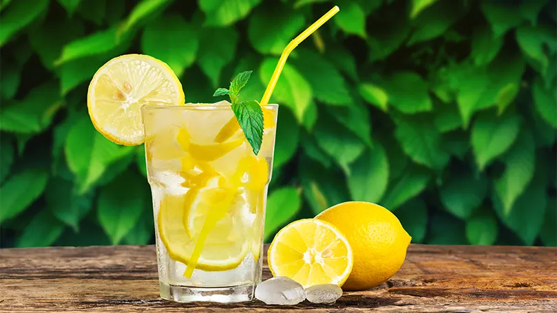 un vaso de agua con limón junto a dos limones sobre una mesa.