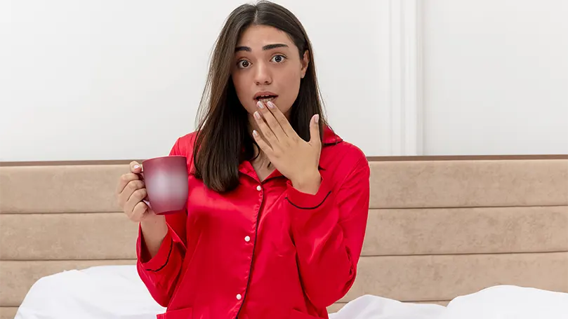 Imagen de una mujer en pijama rojo bebiendo agua al despertarse por sequedad bucal.