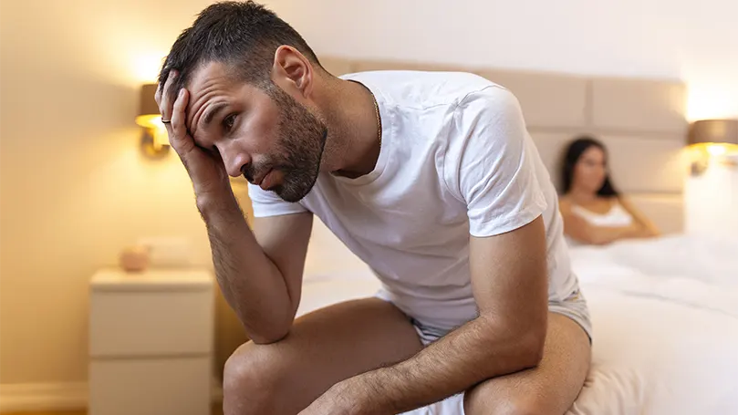 An image of a man sitting on the edge of bed.