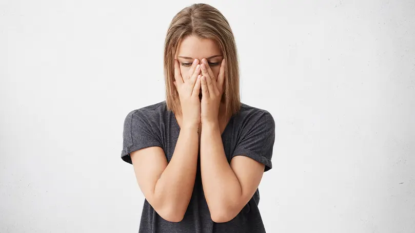 Imagen de una mujer con las manos cubriéndose la cara mientras sufre los síntomas de la fatiga invernal.