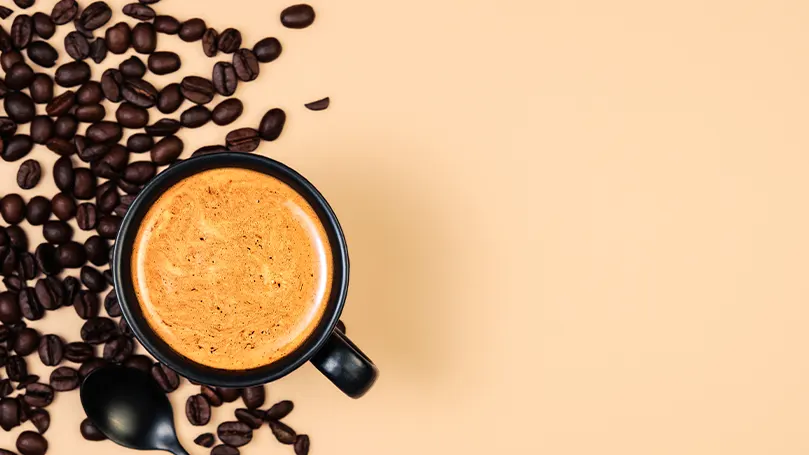 An image of a cup of cofee with cofee beans on the side