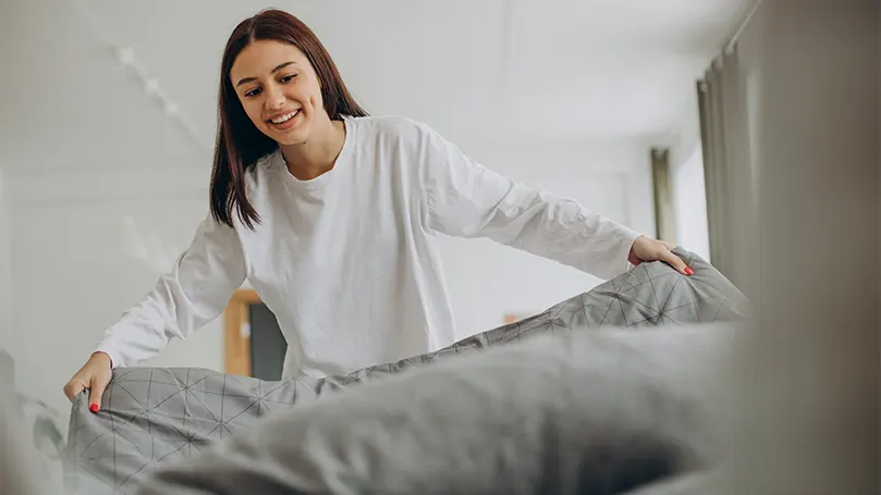 Una imagen de una mujer feliz haciendo su cama.