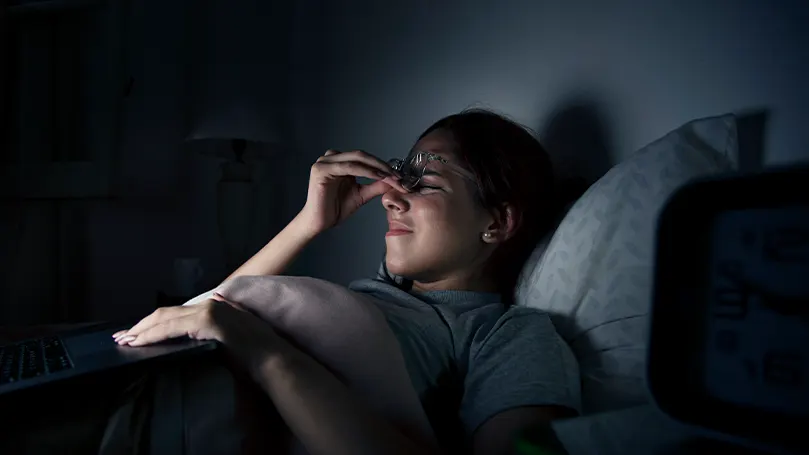 Una imagen de una mujer en la cama por la noche sujetándose la cara por el dolor