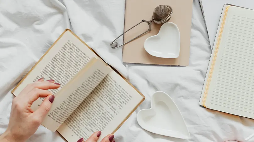 Imagen de una persona leyendo un libro en la cama.