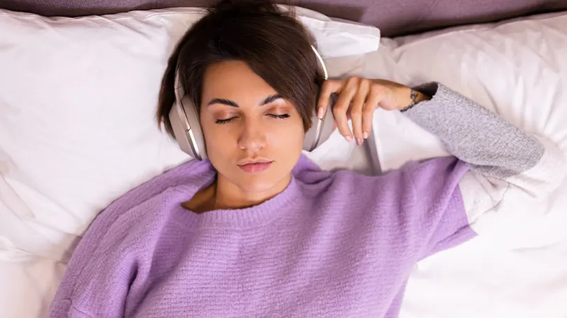 Una imagen de una mujer en la cama con los auriculares puestos