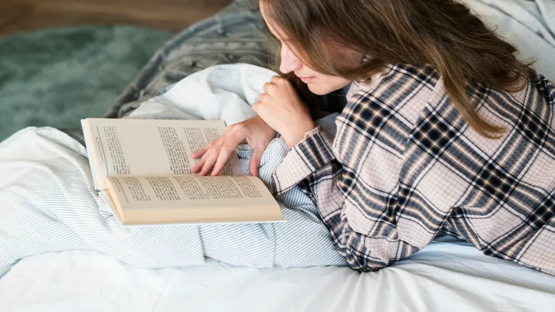 Imagen de una mujer leyendo un libro en la cama.