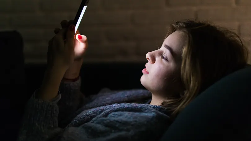 Una imagen de una chica mirando el móvil mientras está en la cama