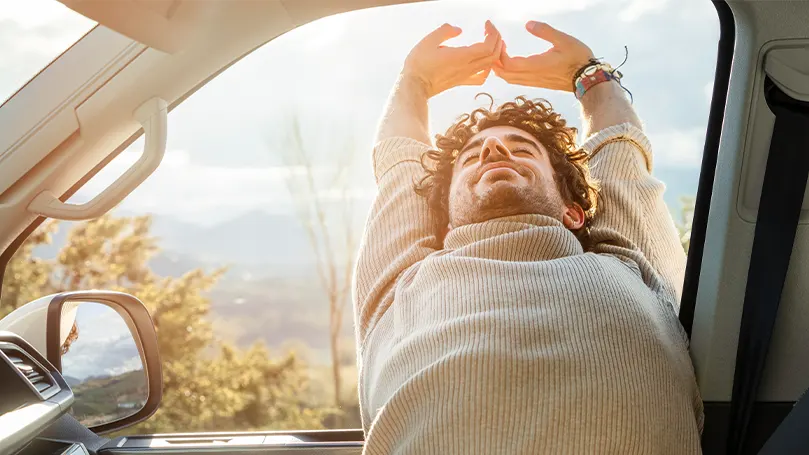 An image of a man stretching after sleeping in a car.