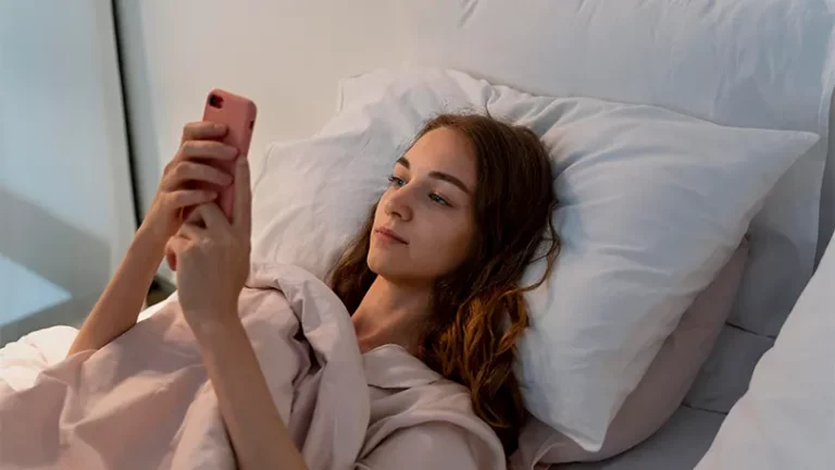 An image of a young woman in bed holding a phone