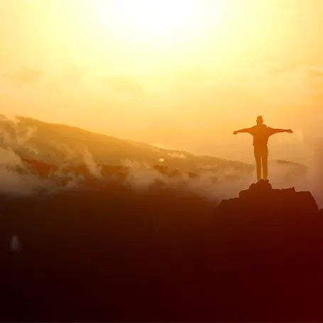 La imagen de un hombre en lo alto de una montaña con la cara iluminada