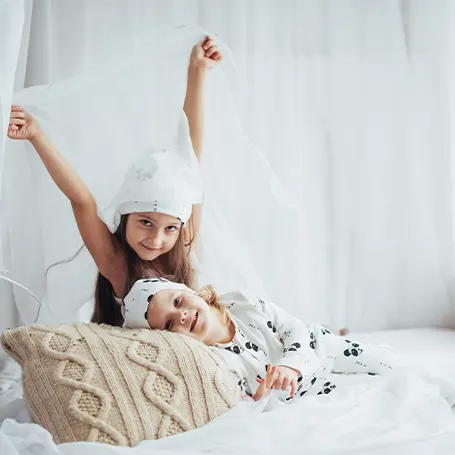 Una imagen de dos niños en la cama con una almohada