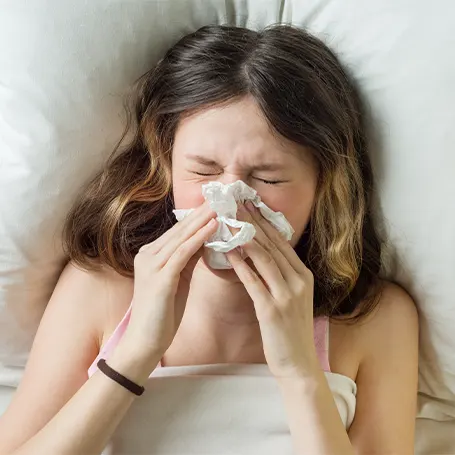 Una imagen de una mujer llevándose un pañuelo a la nariz después de que la ropa de cama le provocara alergia.